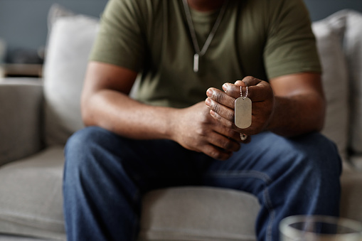 Closeup of African American man as army veteran holding dog tags necklace in hands during therapy session.